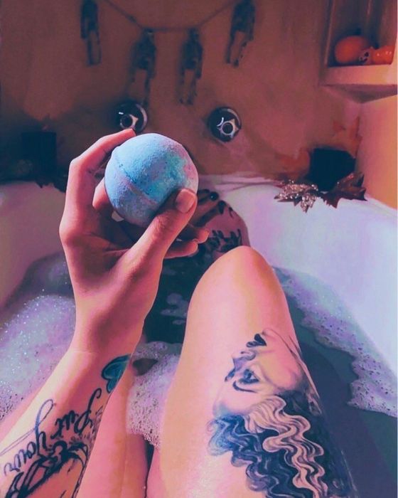 A reviewer enjoys a relaxing moment in a colorful bath, holding a bath bomb.
