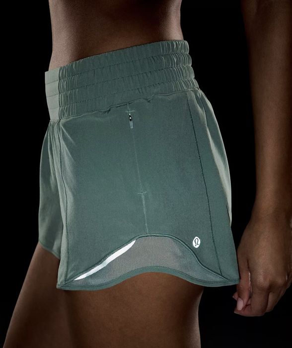 Close-up of someone wearing green, form-fitting sporty shorts with a small Lululemon logo, set in a dark environment.