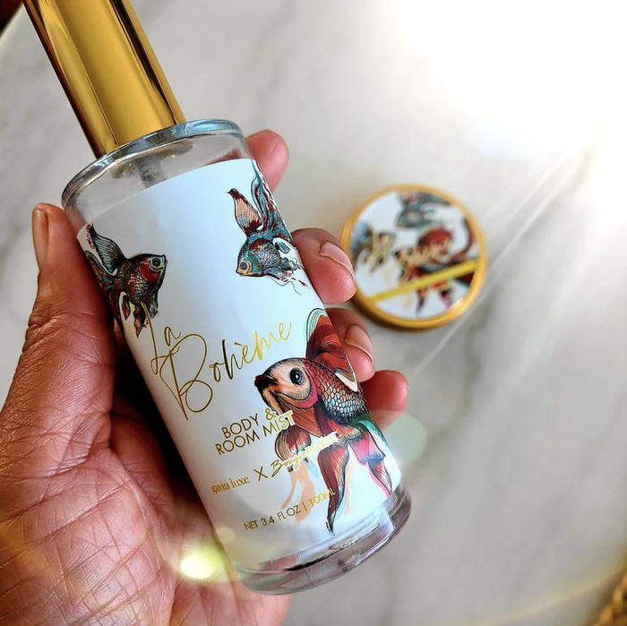 A hand is holding a bottle of body and room mist.