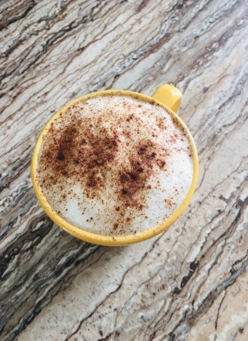 A reviewer shows off a latte topped with a frothy foam layer, dusted with cinnamon for a touch of spice.