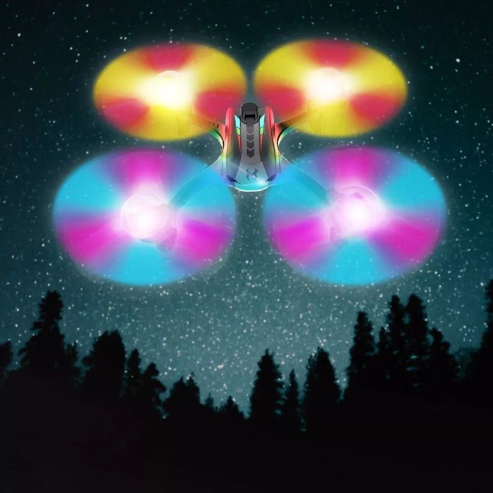 A quadcopter drone with multicolored, glowing propellers soars above a forest beneath a starry sky.