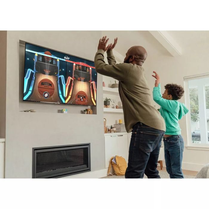 Two people enthusiastically play a basketball video game on a TV in the living room, raising their hands in the air to interact with the game.