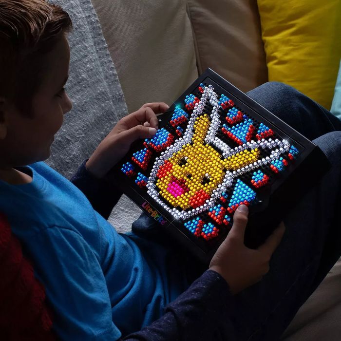 A child holds up a Lite-Brite creation featuring a Pikachu design