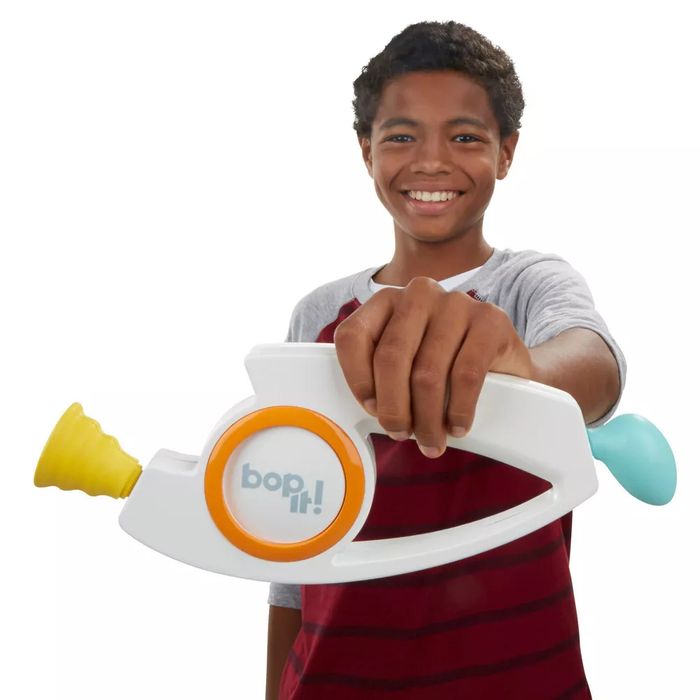 A boy grins as he holds a Bop It! toy, which features a vibrant yellow, orange, and light blue design.