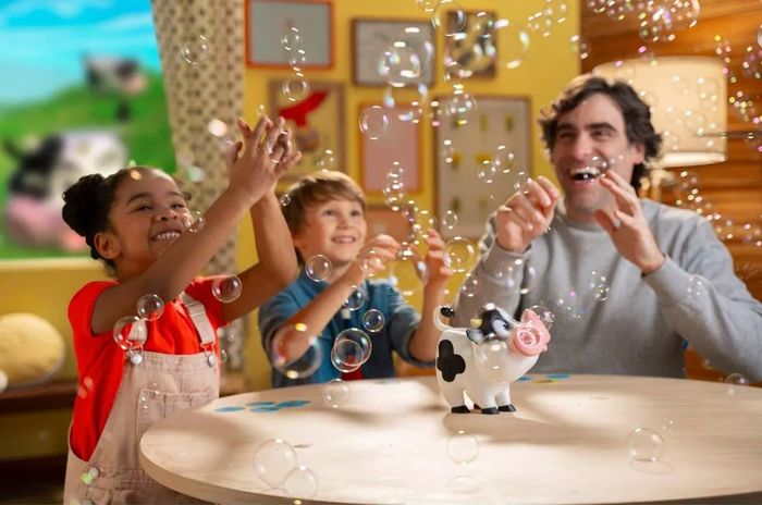 A man and two children are joyfully playing with bubbles and a cow-shaped bubble toy, creating an indoor burst of fun and laughter.