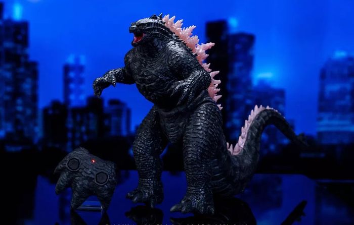 A Godzilla toy figure stands against a cityscape backdrop, complete with a matching remote control
