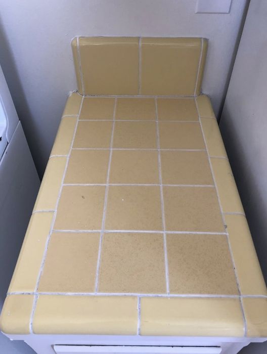 A yellow tiled countertop with a small raised back section, next to a white appliance