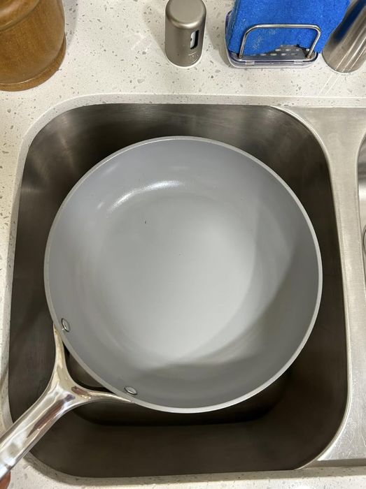 A large ceramic frying pan sitting in a kitchen sink, waiting to be washed