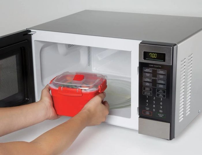 A pair of hands placing a hot, red container along with its lid into a microwave.