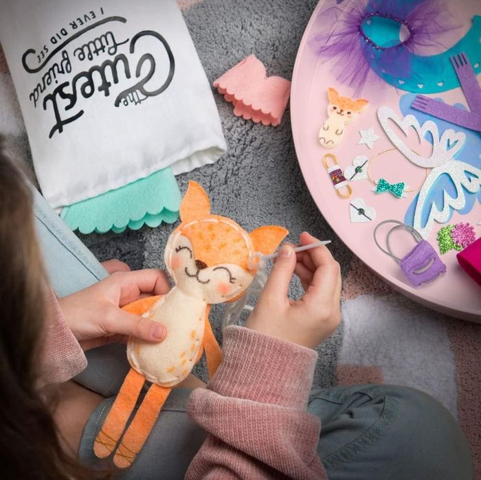 A child model sewing a fox-shaped plush doll, surrounded by various craft supplies.