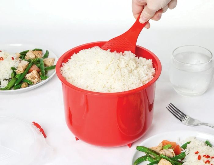 A red rice cooker brimming with rice, accompanied by a paddle scooping out a portion