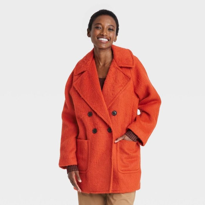 a person wearing a cozy, oversized orange fuzzy lapel coat with extra large front pockets
