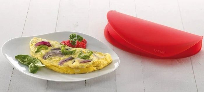 A fluffy omelet served on a plate alongside a vibrant red silicone cooking mold