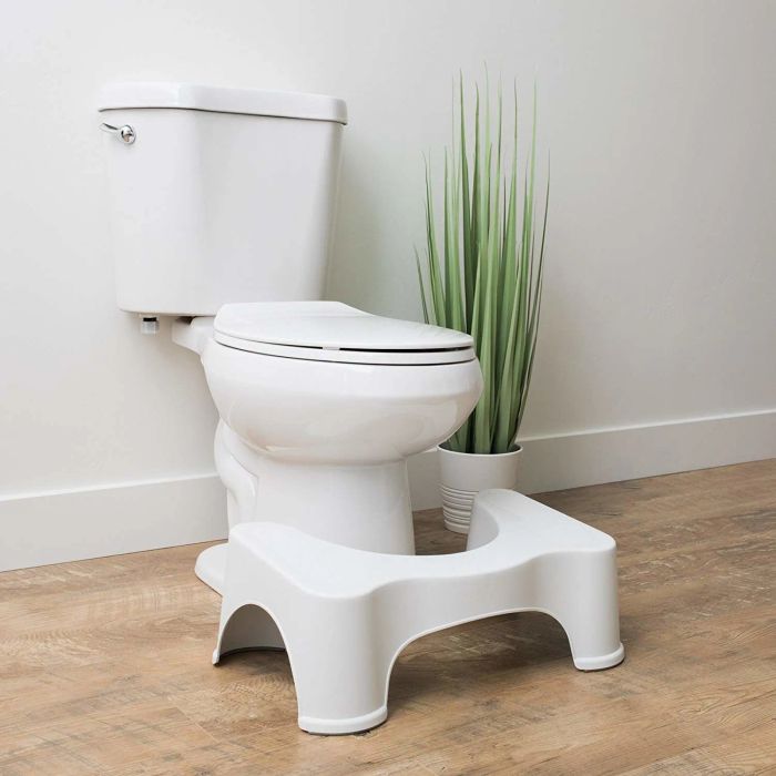 The white Squatty Potty, a u-shaped stool positioned conveniently in front of a toilet