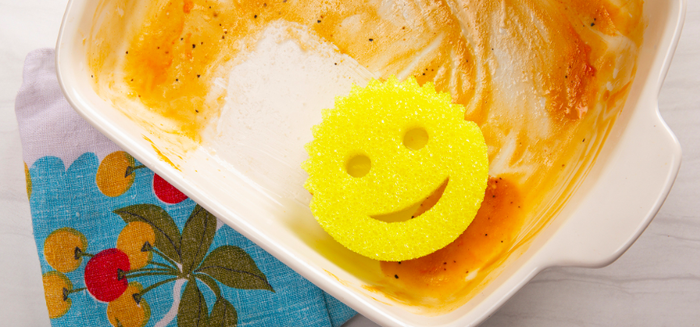 A Scrub Daddy sponge being used to scrub a greasy casserole dish