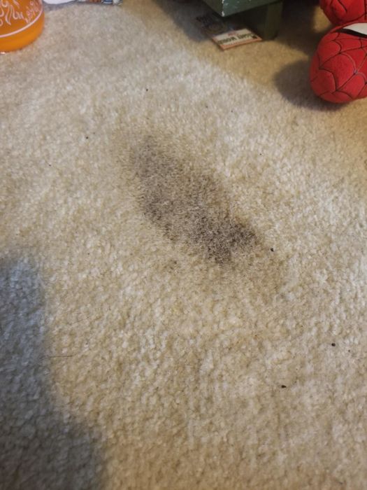 A beige carpet with a brownish-gray stain located in the center of the image.