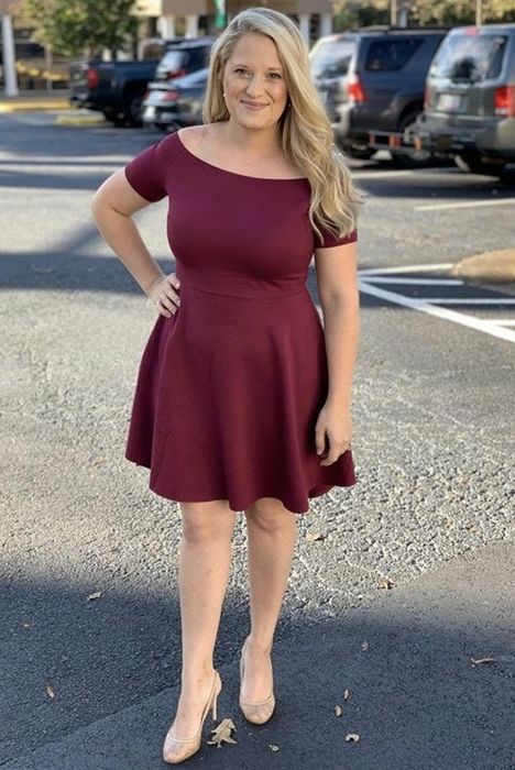 A reviewer wearing a deep maroon cocktail dress.