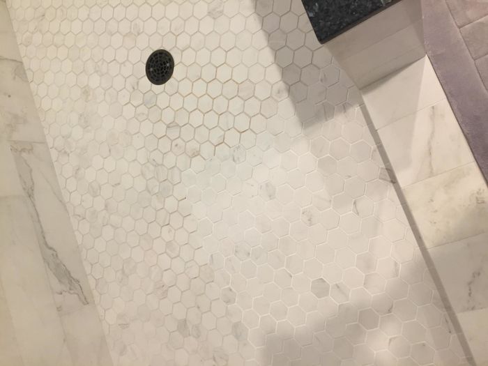 A reviewer’s photo showing half of their shower’s grout lines restored after using the grout-cleaning pen