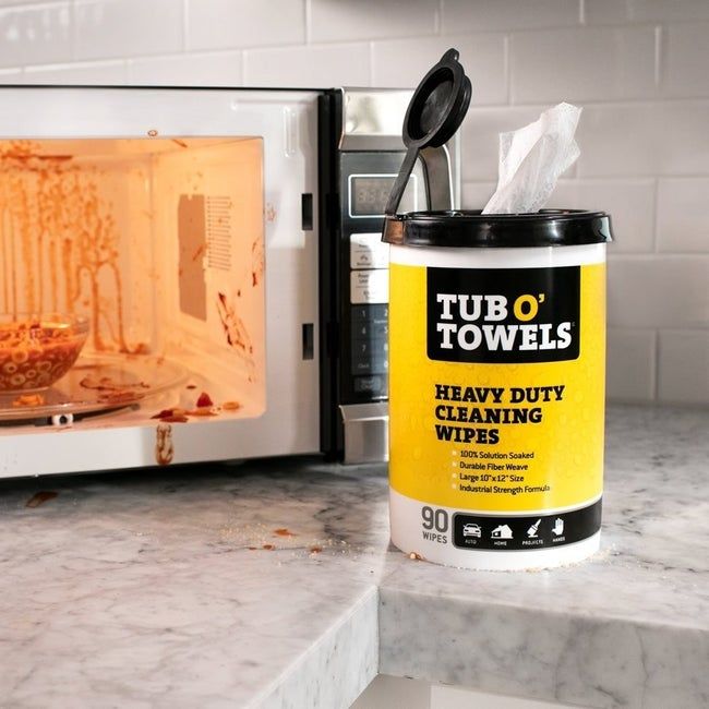 A canister of cleaning wipes placed next to a messy microwave