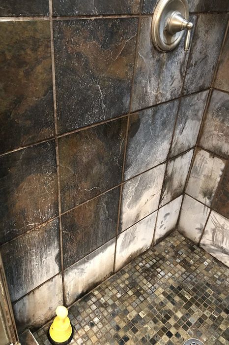 A reviewer's photo showcasing their tiled shower covered in soap scum and hard water stains