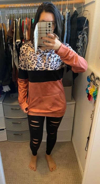 A mirror selfie captures someone in a leopard print and color-block hoodie paired with ripped black leggings, standing in a closet.