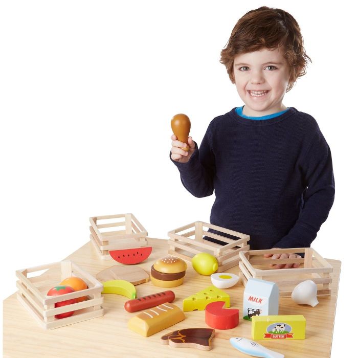 A child holding a drumstick surrounded by various play foods.