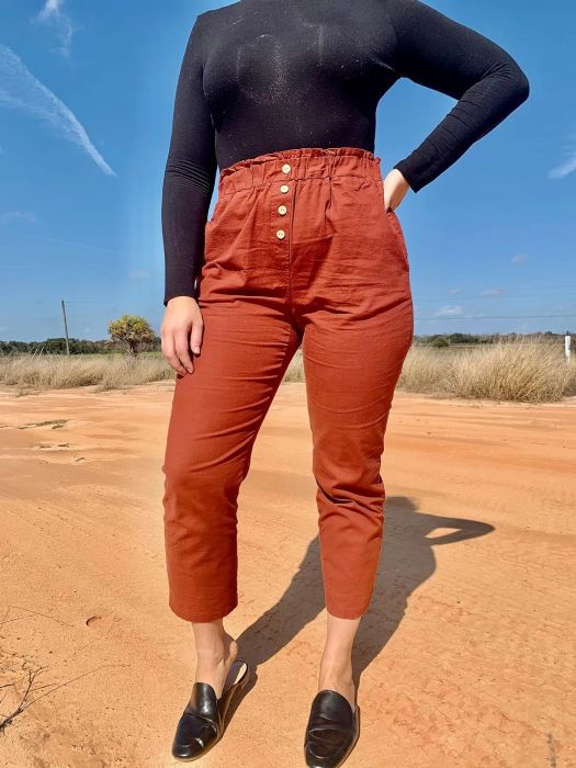 A reviewer wearing rust-colored pants with a black shirt tucked in for a sleek look.