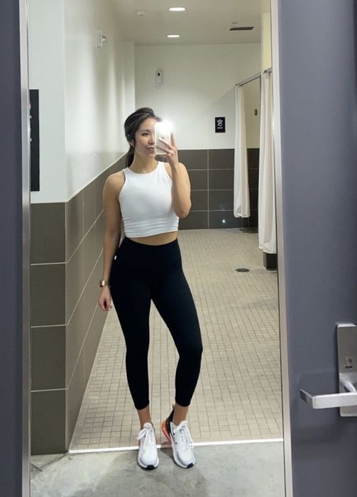 A reviewer taking a mirror selfie while wearing a white tank top.