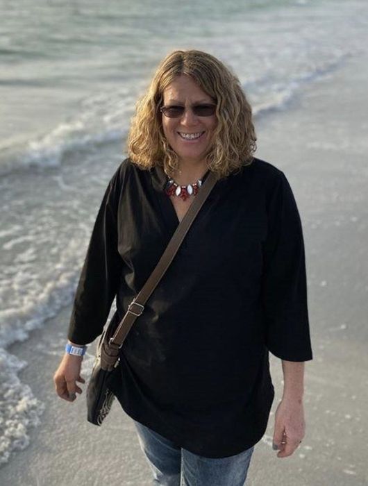 A reviewer walking on a beach wearing a black tunic shirt.