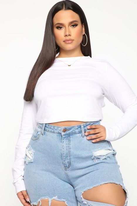 plus-size model wearing a white long-sleeve crop top and ripped jeans