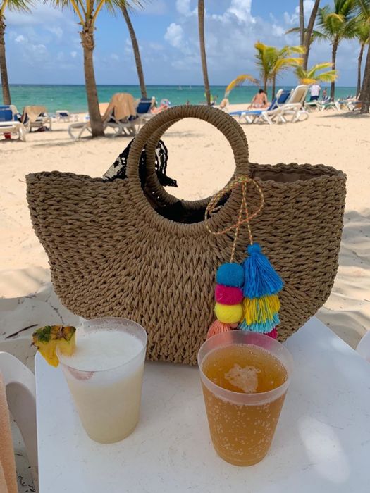 The purse resting beside two tropical beverages on a sandy beach.