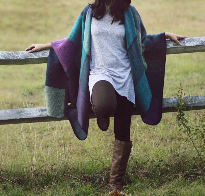 A customer review photo of them wearing the cozy poncho in a serene meadow.