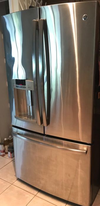 A reviewer shows their stainless steel refrigerator before cleaning, looking dirty and smudged.