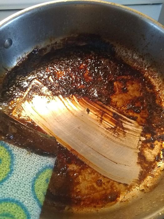 A reviewer's pan with tough, crusted grease, showing a clean spot in the middle after one wipe with a dry sponge following the use of the powerwash spray.