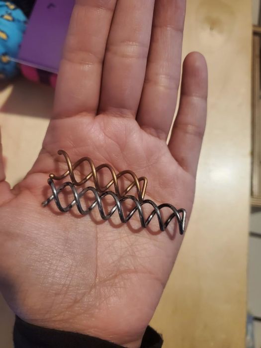 A hand holding two spiral hairpins against a plain background.