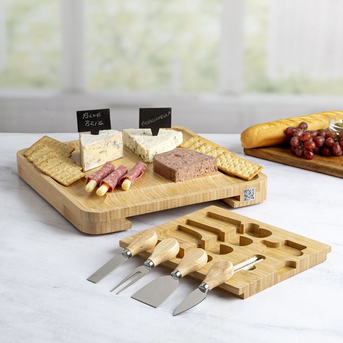 A charcuterie board with food on it, tray removed to reveal the utensils inside