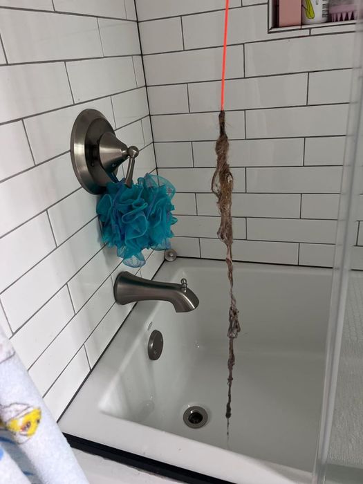 A reviewer's photo showing an orange drain snake that successfully removed large clumps of hair from a shower drain.