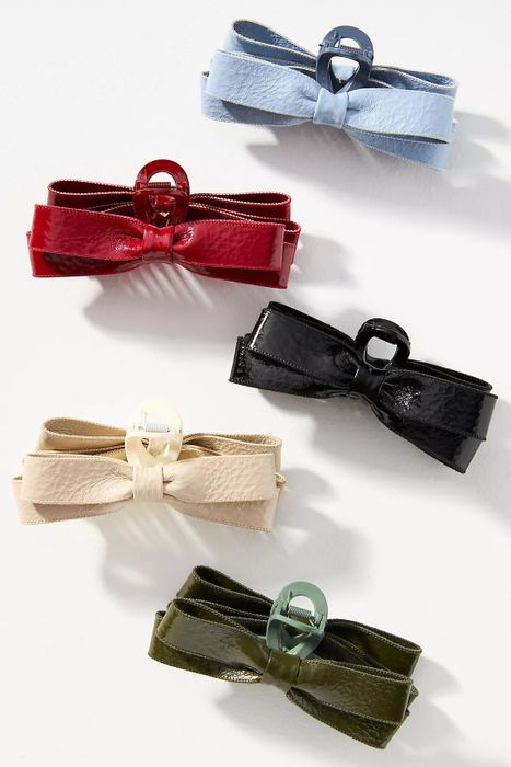 Five leather bow hair clips in shades of red, black, blue, beige, and olive green, elegantly displayed on a white backdrop.