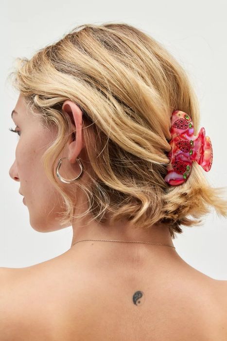 A model with short hair wearing silver hoop earrings and a decorative pink hair clip, embellished with berry details.