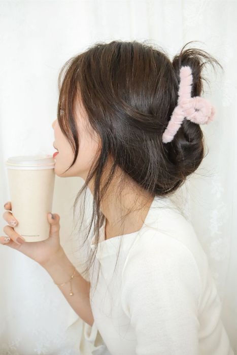 A model wearing a pink teddy hair clip at the back of her head, enjoying a cup of coffee.