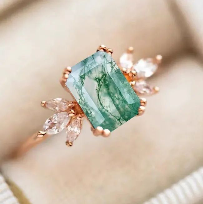 The rose gold band adorned with a swirled green emerald-cut moss agate and six sparkling diamonds