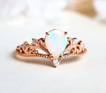 The opal ring features a pear-shaped stone set in a rose gold vintage-style band with intricate swirls and delicate diamonds.