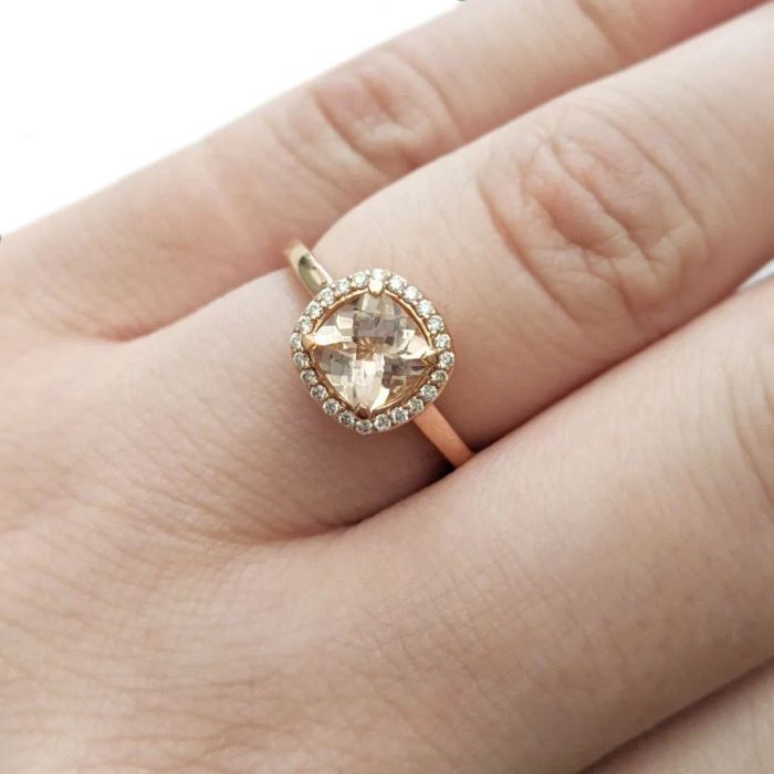 The rose gold ring worn by a model, featuring a cushion-cut morganite stone surrounded by a halo of diamonds