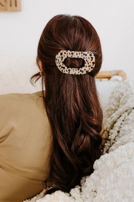 A woman with brown hair wearing a stylish animal print hair clip as she relaxes on a couch.