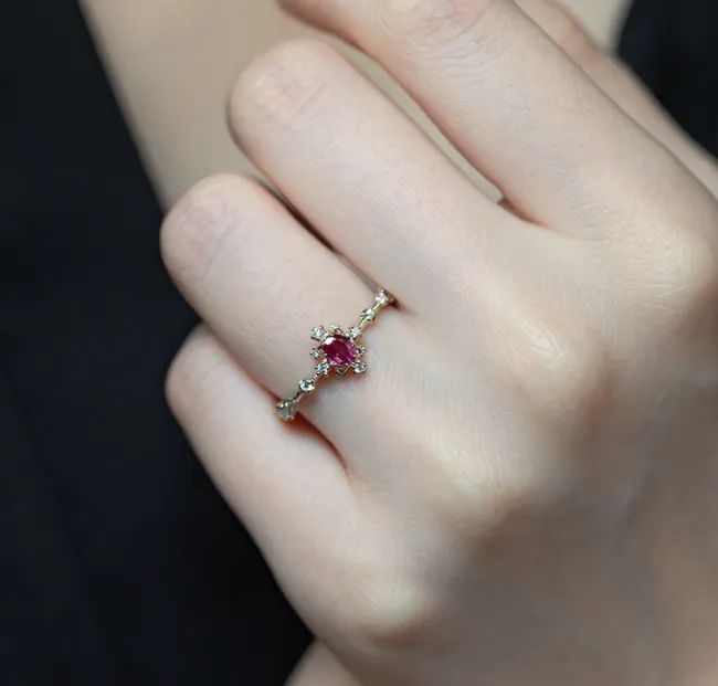 A red diamond ring with four smaller diamonds surrounding the center, and tiny diamonds running down the band.