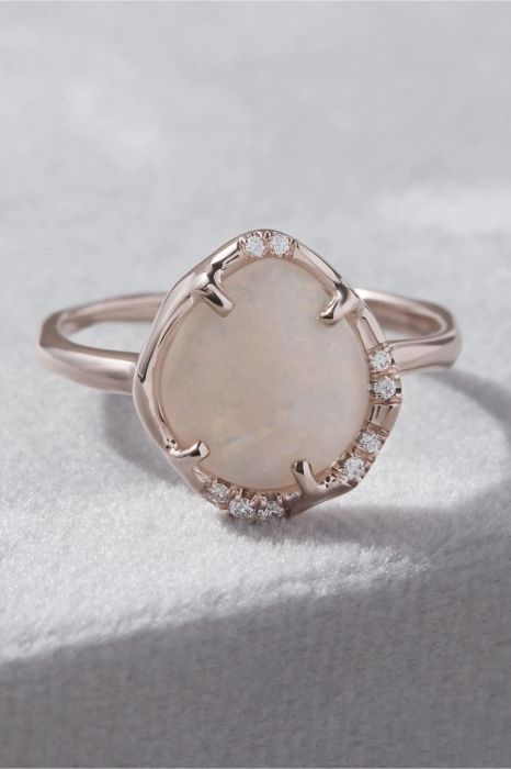 An opal ring surrounded by delicate diamonds, set on an asymmetrical frame that stands out as a truly unique design.