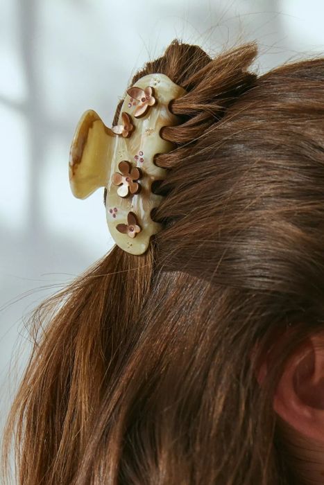 A model with brown hair, adorned with a decorative flower hair clip shaped like a claw.