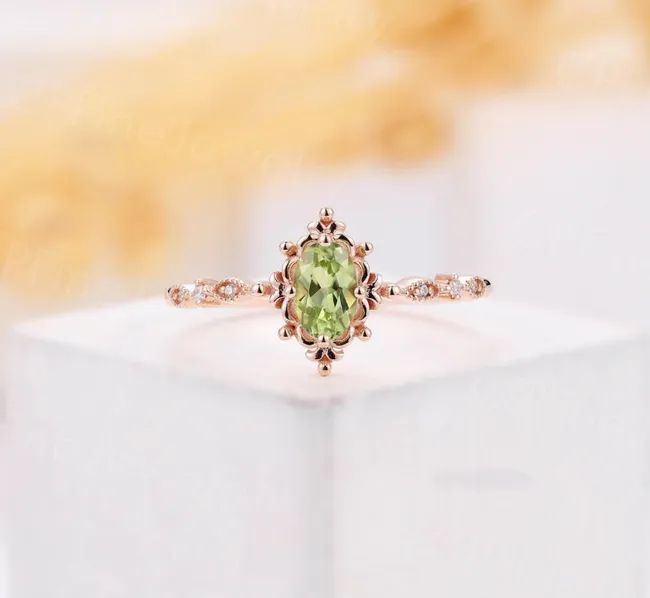 A green peridot ring featuring an oval shape, paired with a rose gold band.