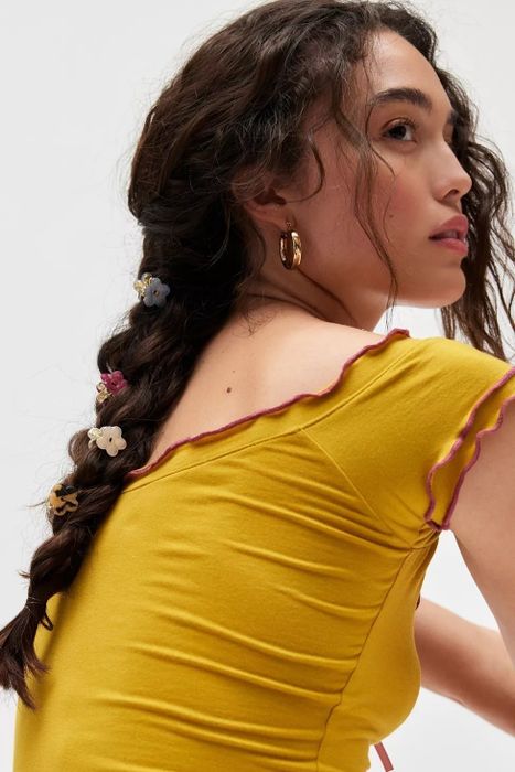 A model sports a braided hairstyle with floral hair accessories, paired with a ruffled top.