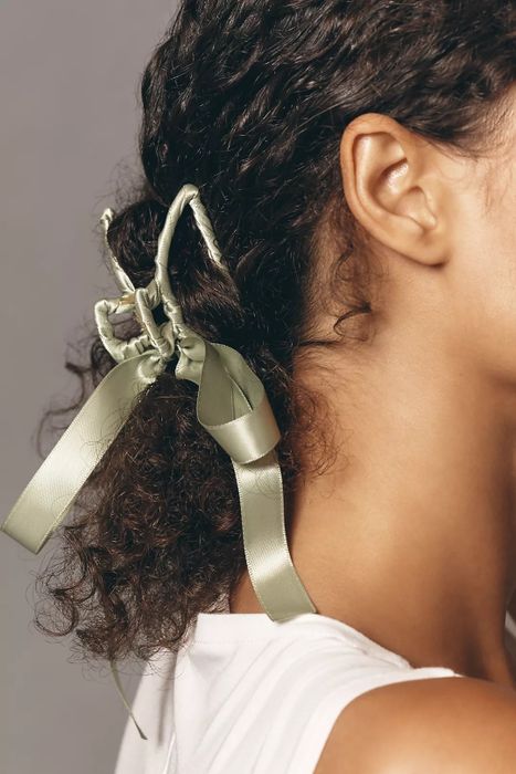 A woman with curly hair styles her hair with a decorative bow accessory.